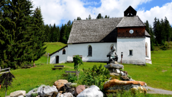 Die St. Agatha Kapelle am Kristberg steht auf einer grünen Almwiese vor dichtem Nadelwald. Das historische weiß verputzte Gotteshaus mit steilem Schin