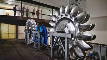 Besuchergruppe blickt von einer Galerie auf Turbinen-Laufräder im Wasserkraftwerk.