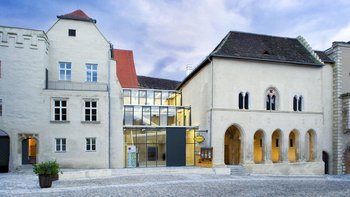 Außenansicht der Gozzoburg, ein Gebäude aus dem Mittelalter, in der Mitte befindet sich ein moderner, gläserner Haupteingang.