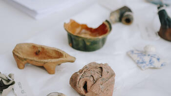 Kleine archäologische Funde liegen auf einem Tisch, darunter ein Porzellan-Schweinchen und ein Schälchen.