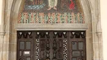 Das Bronzetor mit dem darüberliegenden Mosaik wurde 1981 von Alois Dorn geschaffen. Das Mosaik besteht aus 17.000 venezianischen Glassteinen.